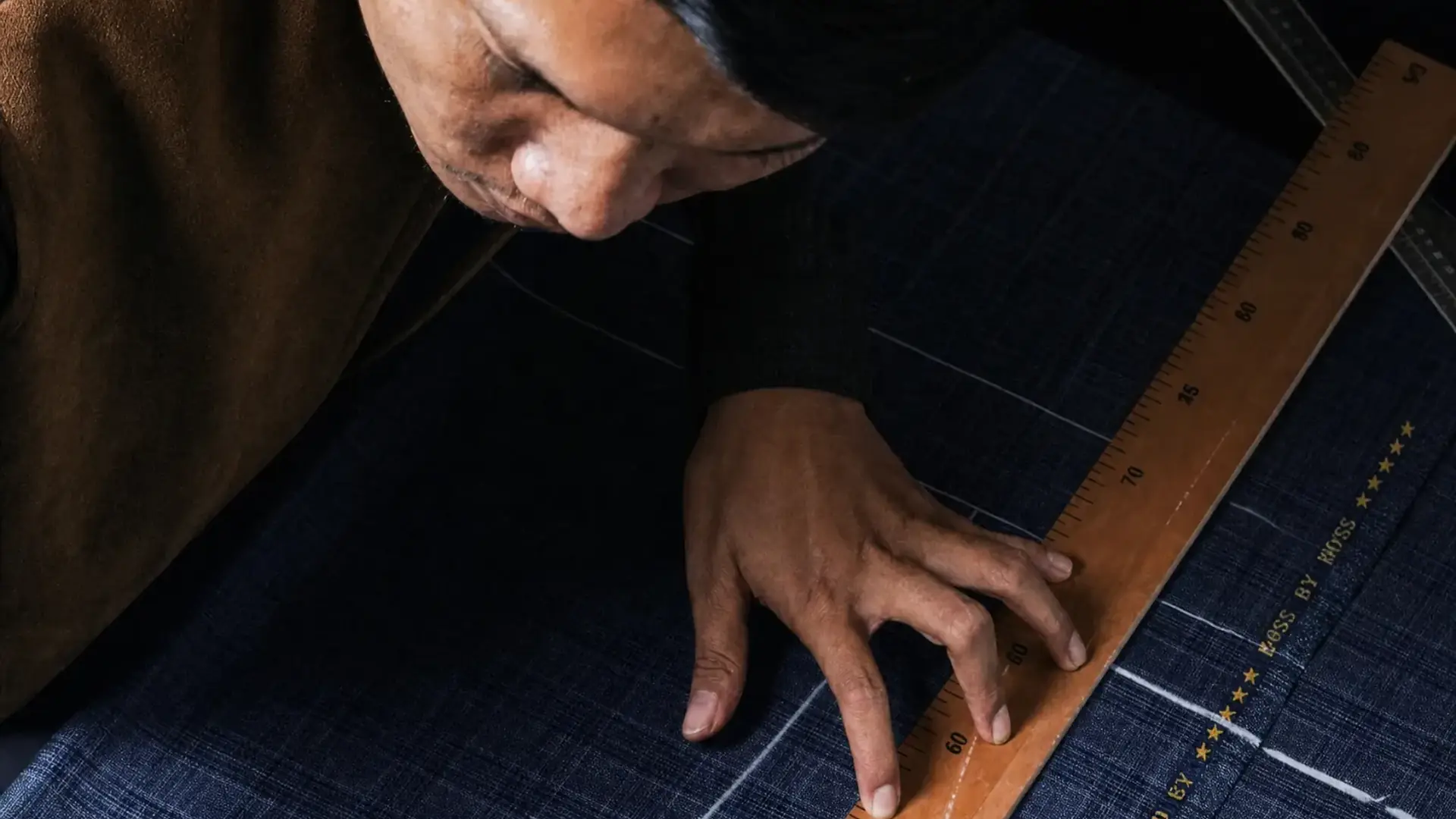Penjahit Tarda menarik garis pola dengan penggaris kayu di atas kain